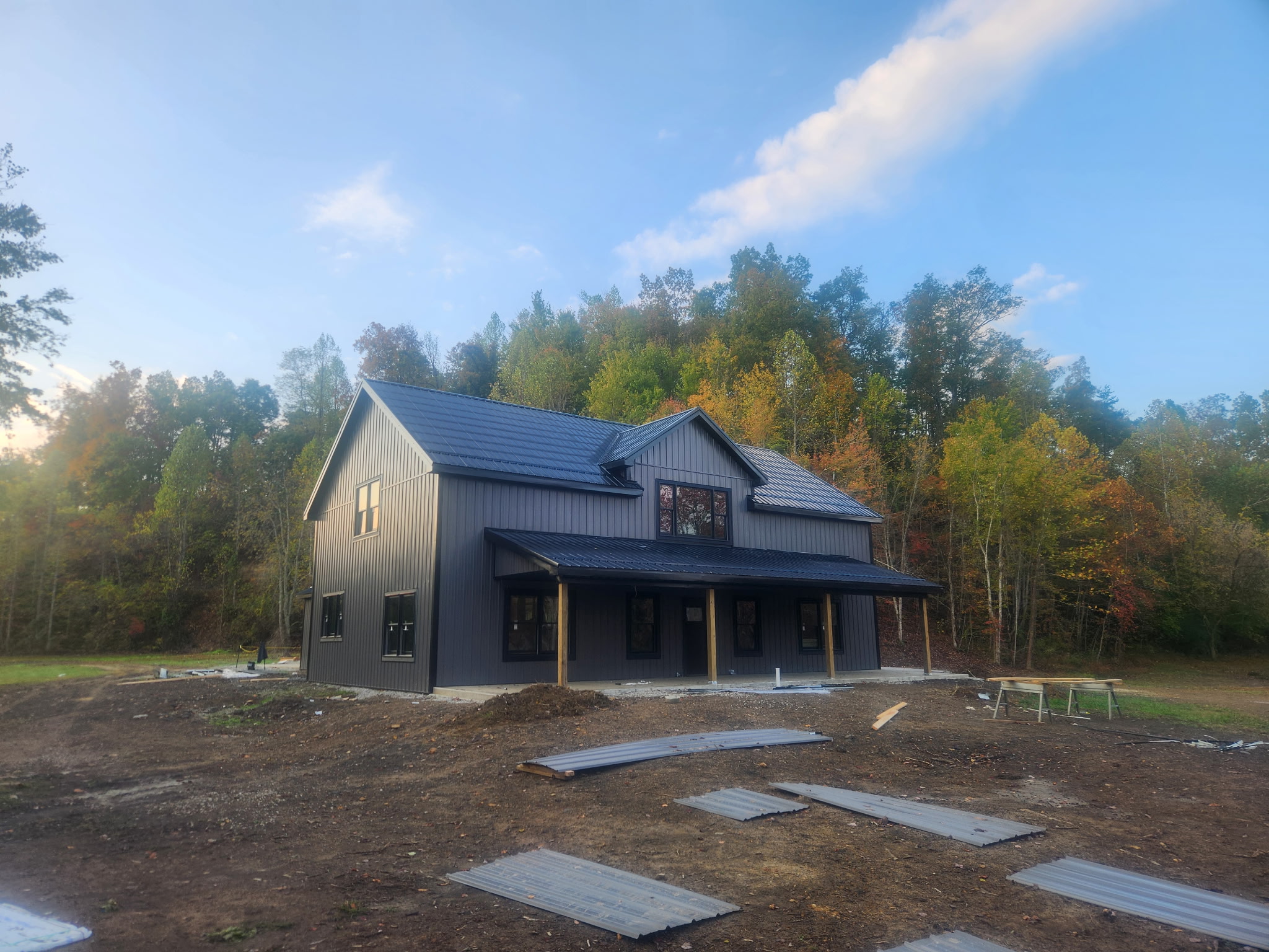 Two-story home with dark metal siding, a metal roof, and a covered front porch under construction